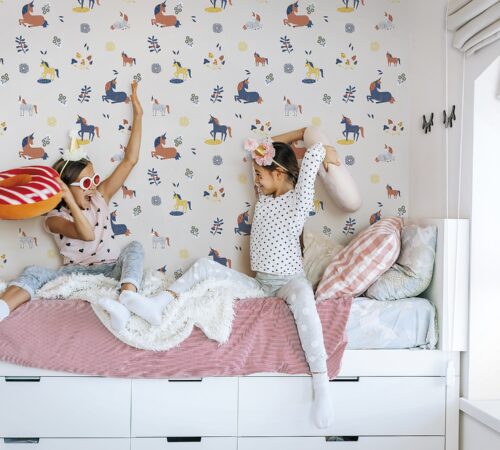 Two children playing together in bed, having fun in bright girly playroom. Kids paljamas party in white bedroom interior.