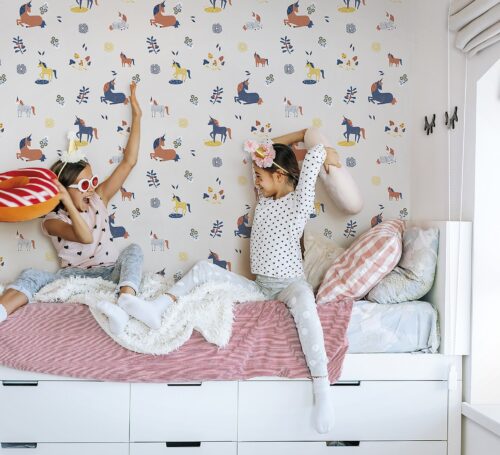 Two children playing together in bed, having fun in bright girly playroom. Kids paljamas party in white bedroom interior.